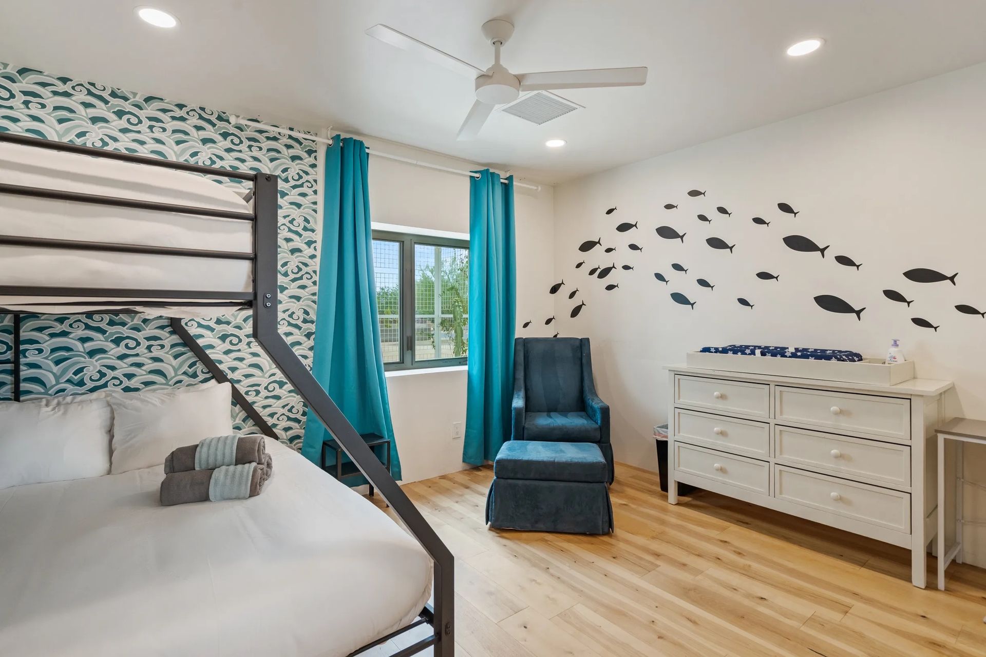 Bedroom with bunk beds, teal curtains, a white dresser with fish decals, and a teal armchair.