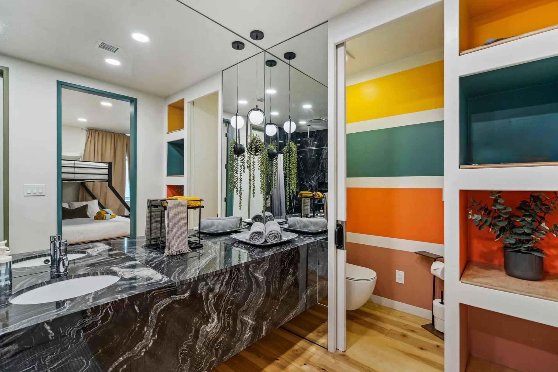 Bathroom with a colorful accent wall, a dark granite countertop, and a mirror reflecting a bedroom with bunk beds.