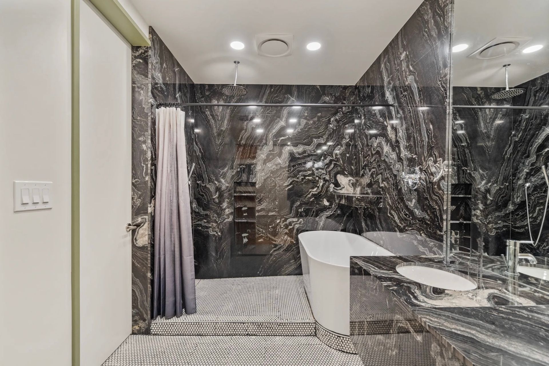 Luxurious bathroom with black marble walls and a patterned tile floor. A white bathtub sits in the center with a glass shower door.