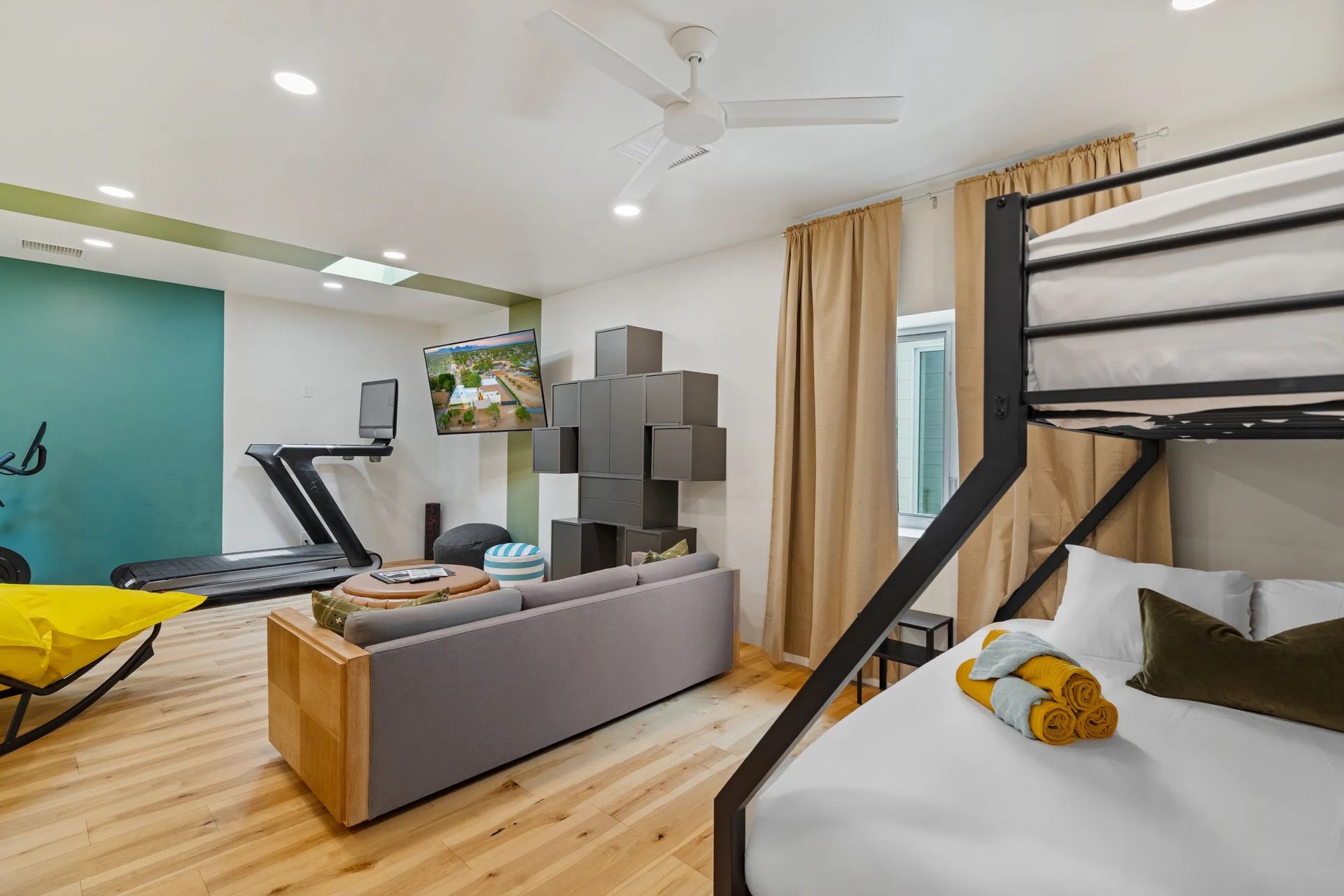 Modern room with bunk bed, sofa, treadmill, and wall-mounted TV. Green and yellow accents with wooden floors and neutral walls.
