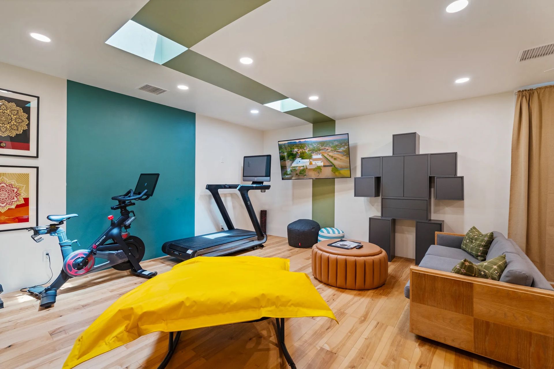 A home gym with a stationary bike, treadmill, and sofa. A large yellow cover sits on a table.