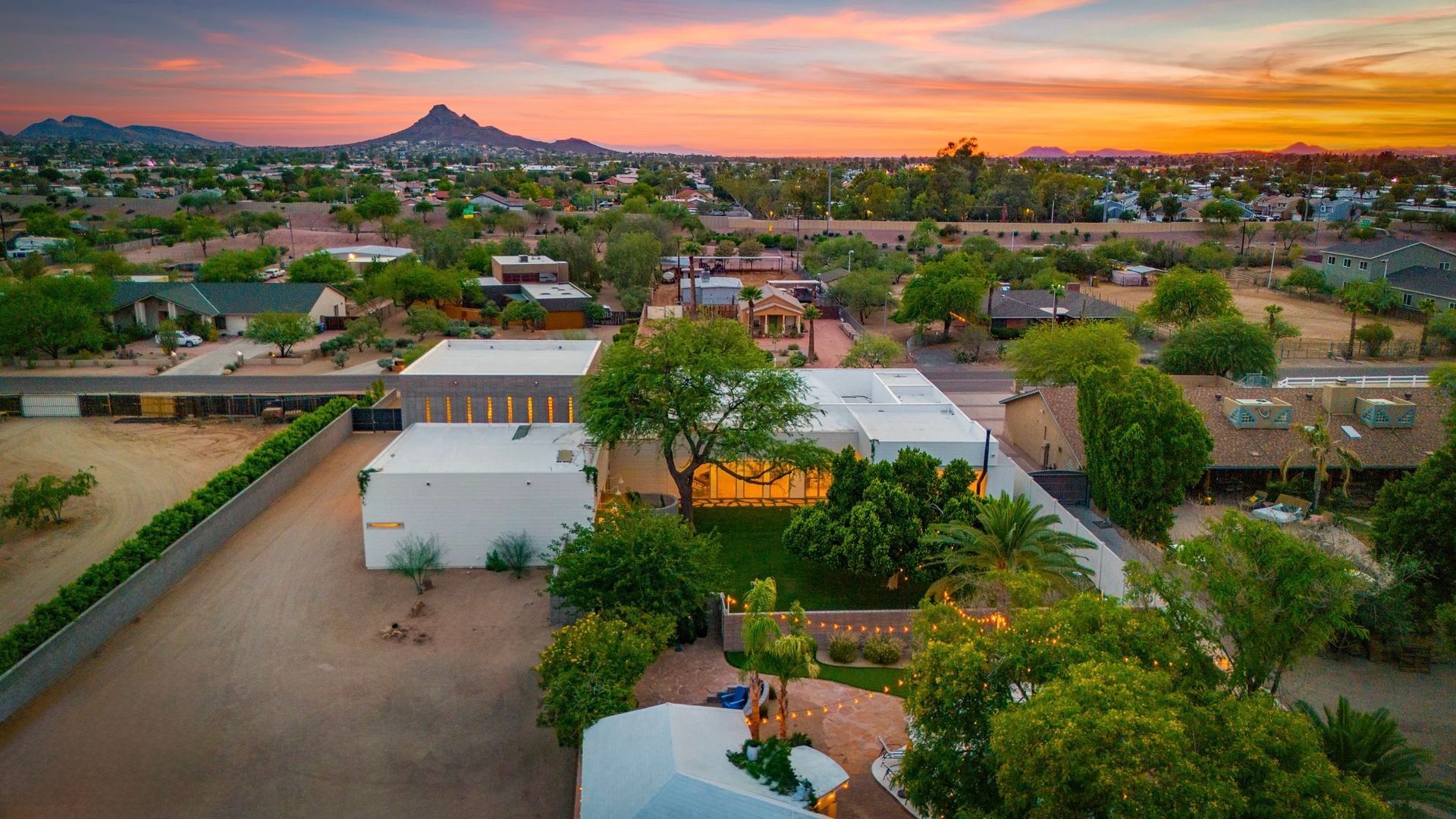 Aerial view of a modern home with a sunset in the background, mountains, and lush green trees.