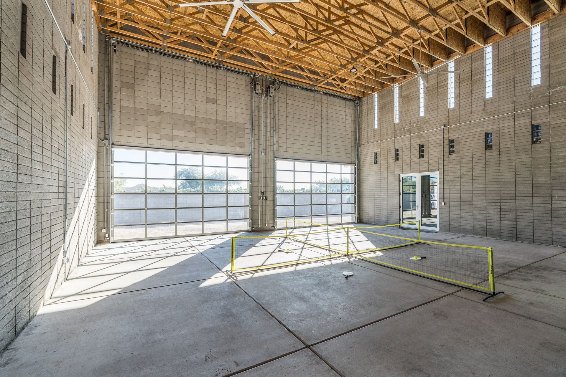 Interior of a large, unfinished building with exposed wooden beams, concrete floor, and garage door style windows.