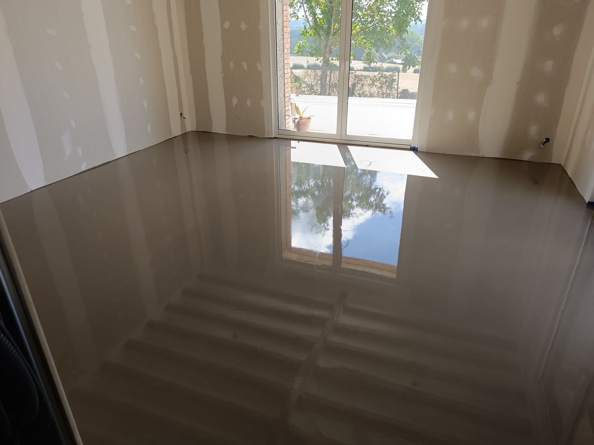 Pièce avec dalle de béton juste coulée et baie vitrée