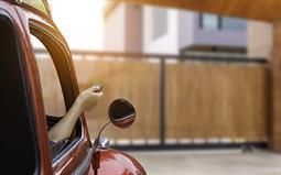 Eine Person fährt ein Auto und öffnet mit einer Fernbedienung ein Garagentor.