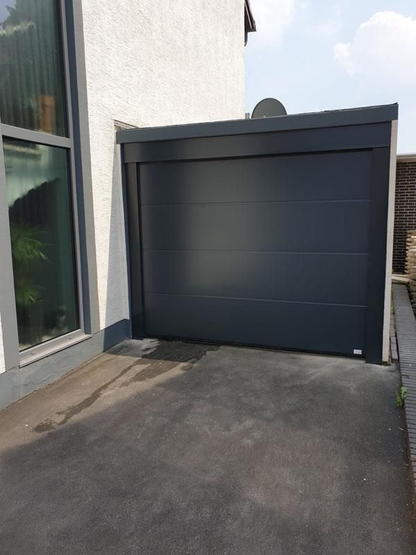 Vor einem weißen Haus steht ein schwarzes Garagentor offen