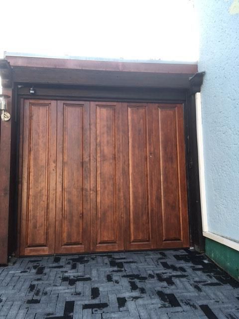 Ein hölzernes Garagentor öffnet sich zu einer gemauerten Auffahrt