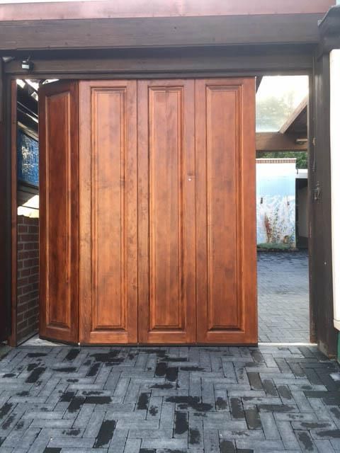 Ein hölzernes Garagentor öffnet sich zu einer gemauerten Auffahrt