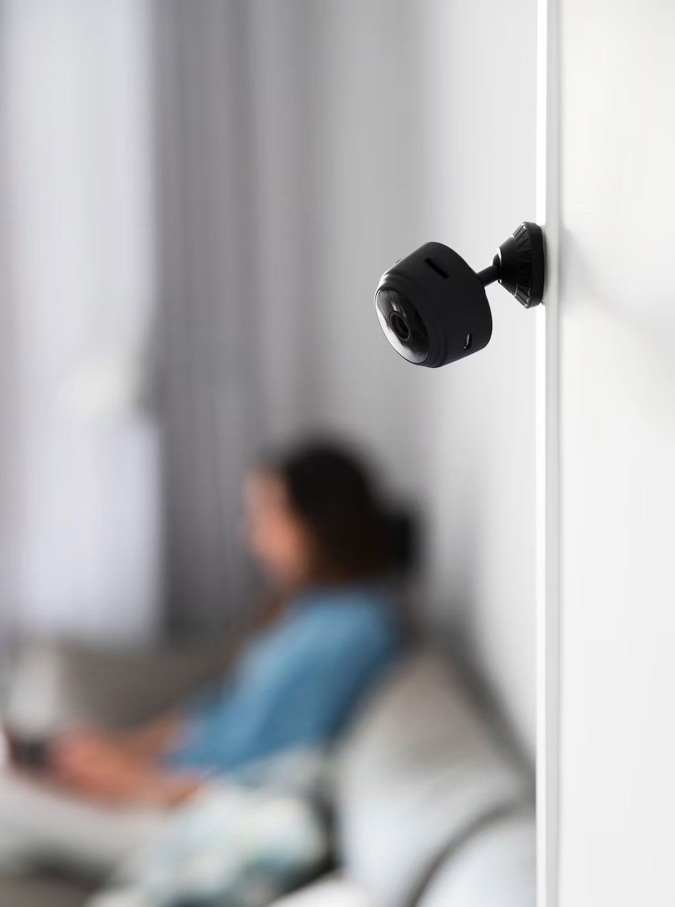Una cámara de seguridad negra montada en la pared enfoca a una persona borrosa sentada en un sofá.