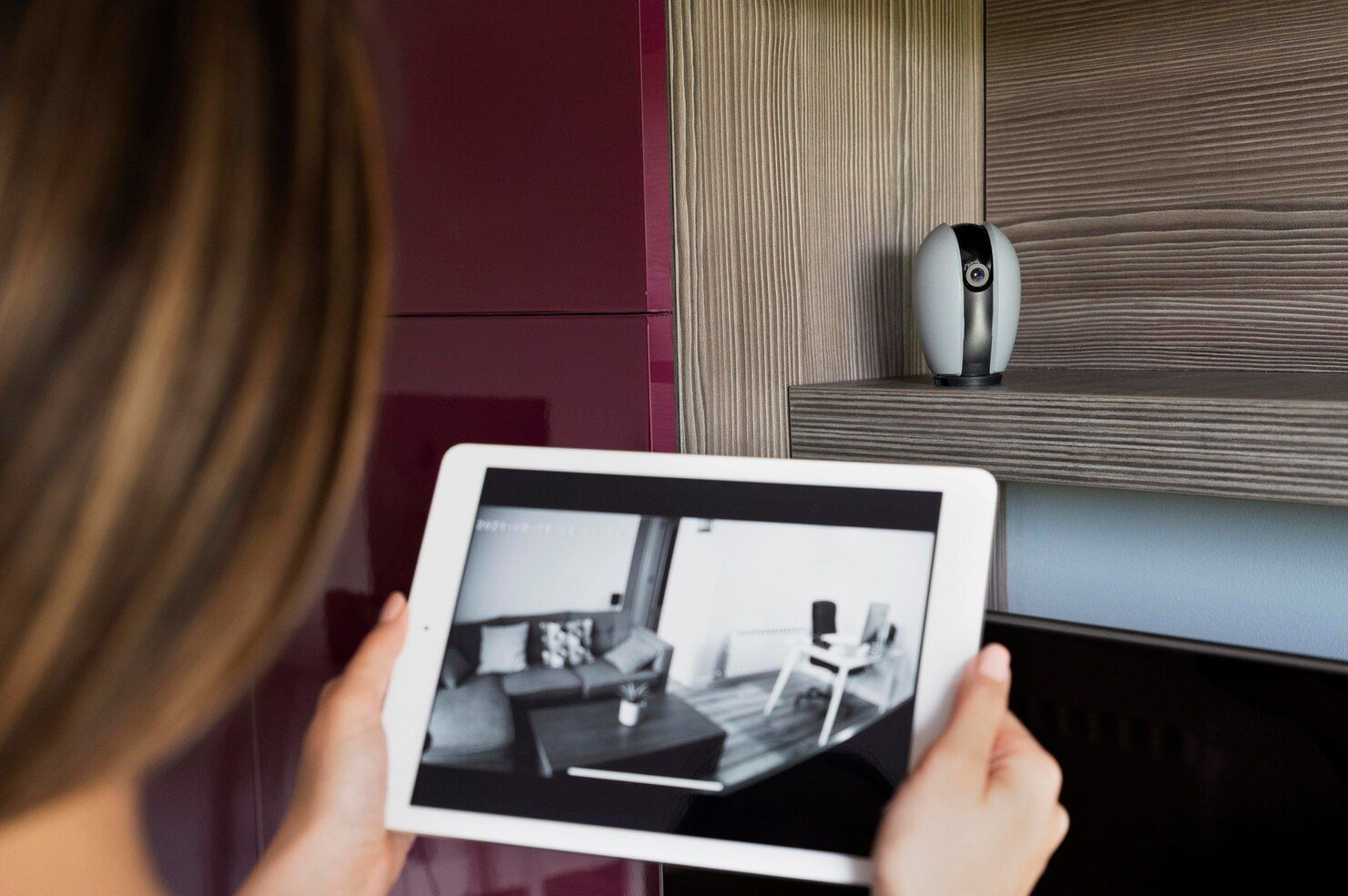 Una persona sostiene una tableta que muestra una vista en blanco y negro de una sala de estar con una cámara sobre una mesa cercana.