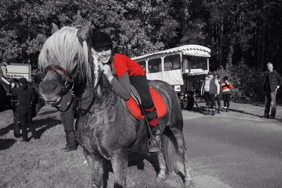 Mädchen mit Reiterhelm kuschelt sich an das Pferd beim Reiten