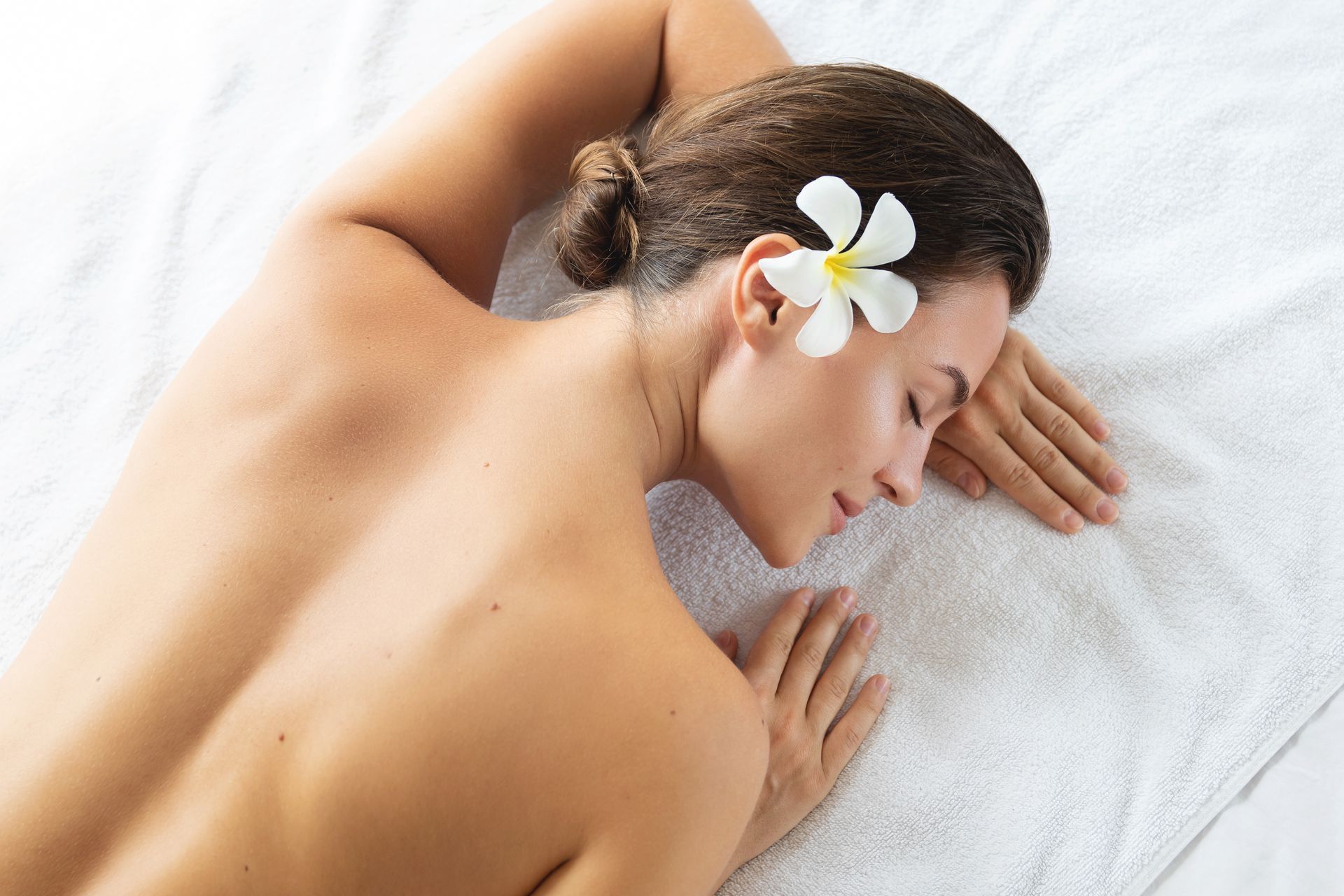 Personne allongée face contre terre sur un lit de spa, se reposant avec une fleur dans les cheveux.