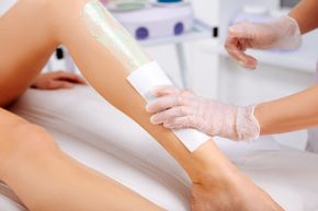 Des mains gantées appliquent de la cire sur la jambe d'une cliente dans une salle de soins d'un spa.