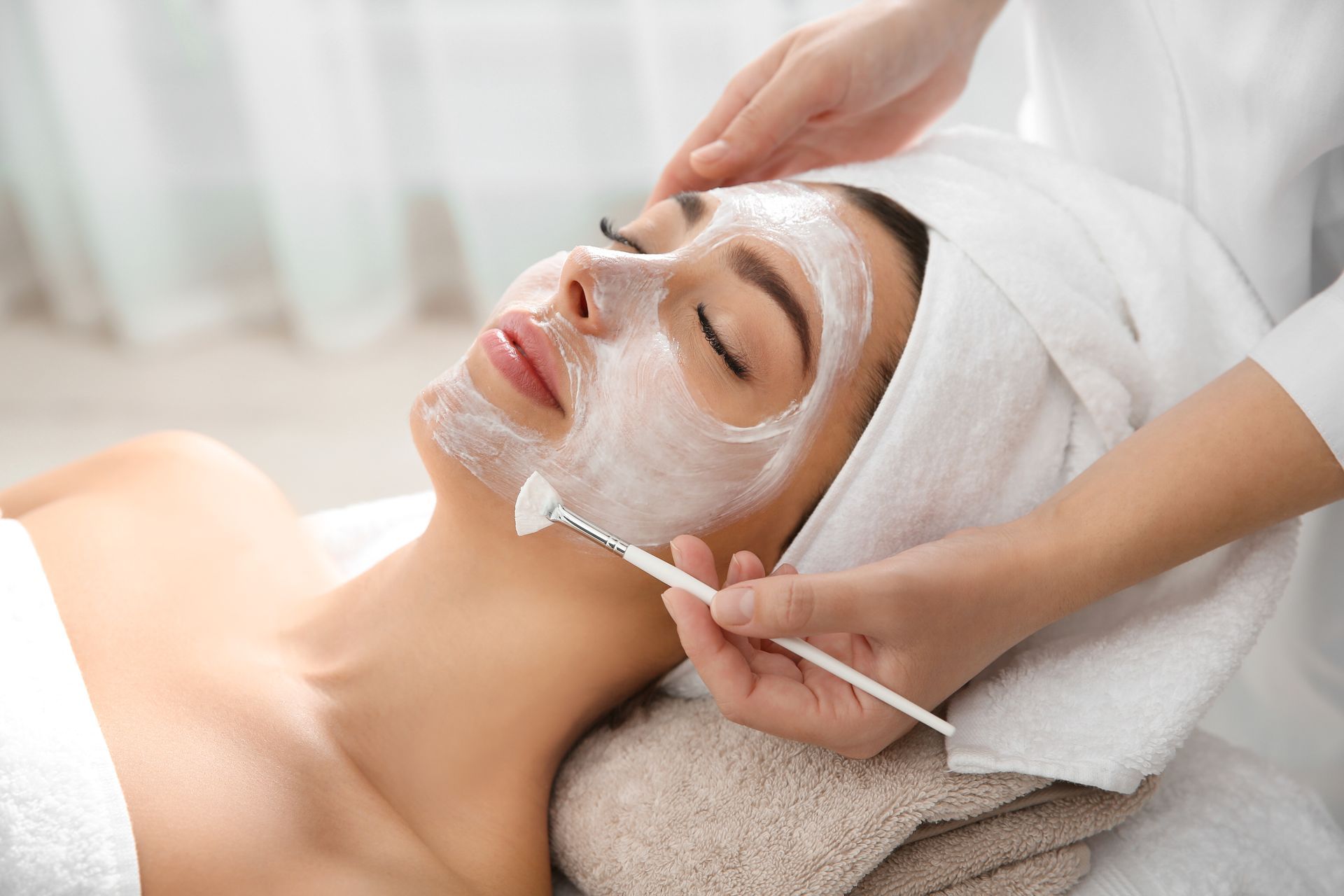 Soin du visage en institut avec application de crème sur le visage d'une femme par un(e) praticien(ne).