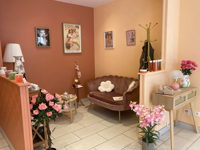 Salle d'attente confortable avec des fleurs, une chaise et des tableaux encadrés sur des murs.