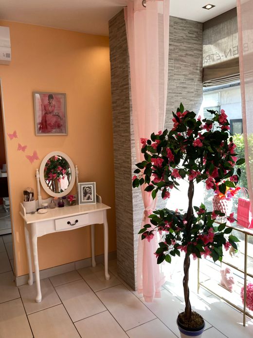 Couloir avec une petite table, des décorations murales et un arbre fleuri en pot près d'une fenêtre lumineuse.