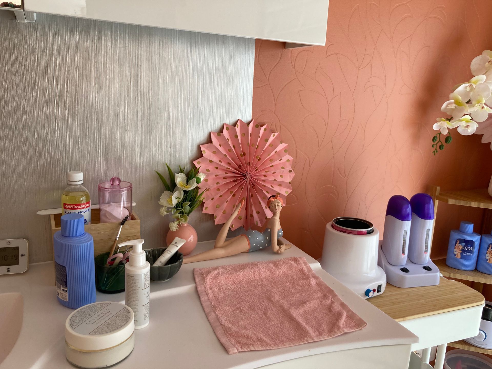 Coiffeuse avec cosmétiques, petit miroir, fleurs et articles de toilette sur un bureau.