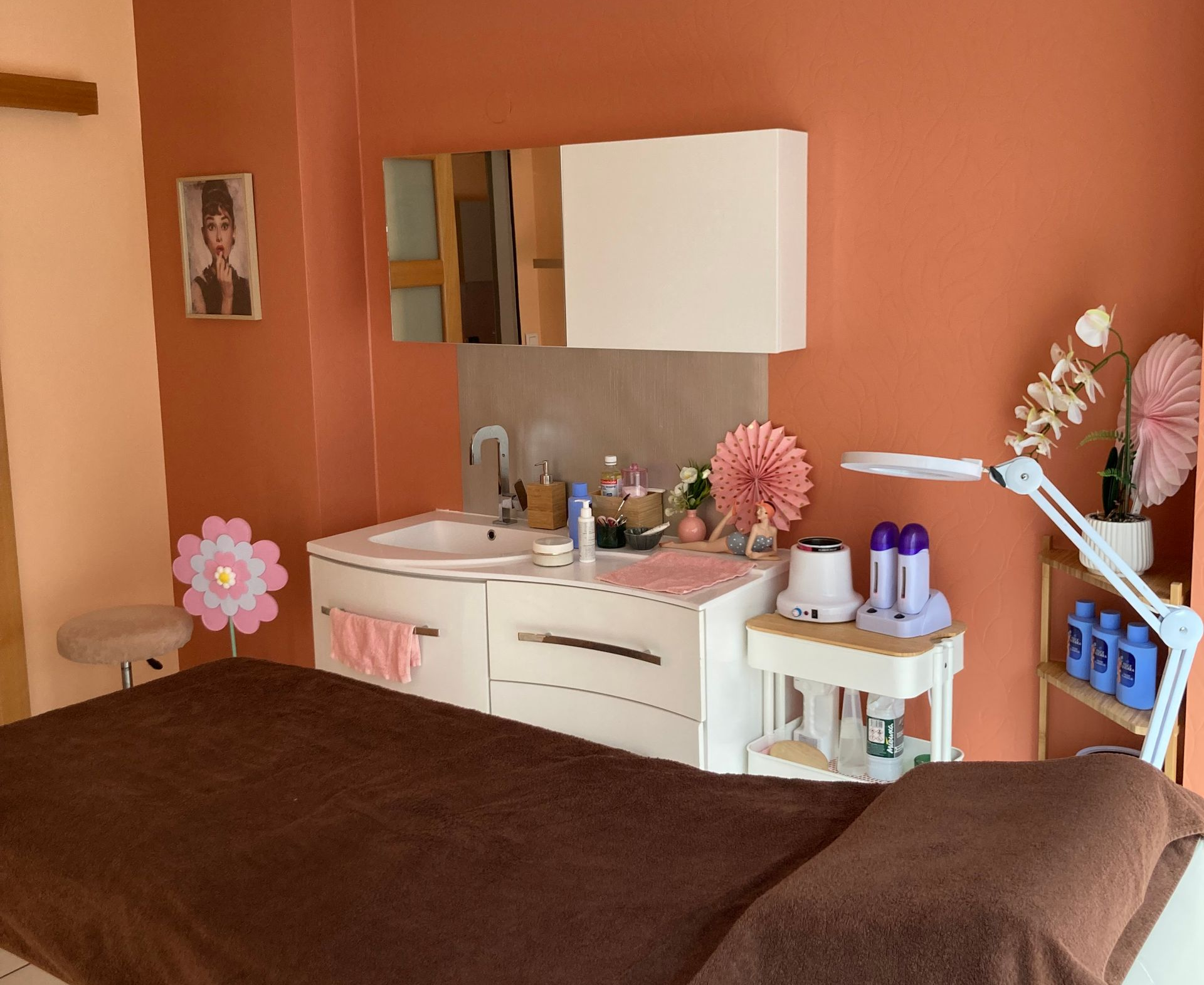 Salle de soins spa avec table de massage, lavabo, miroir et décoration florale.