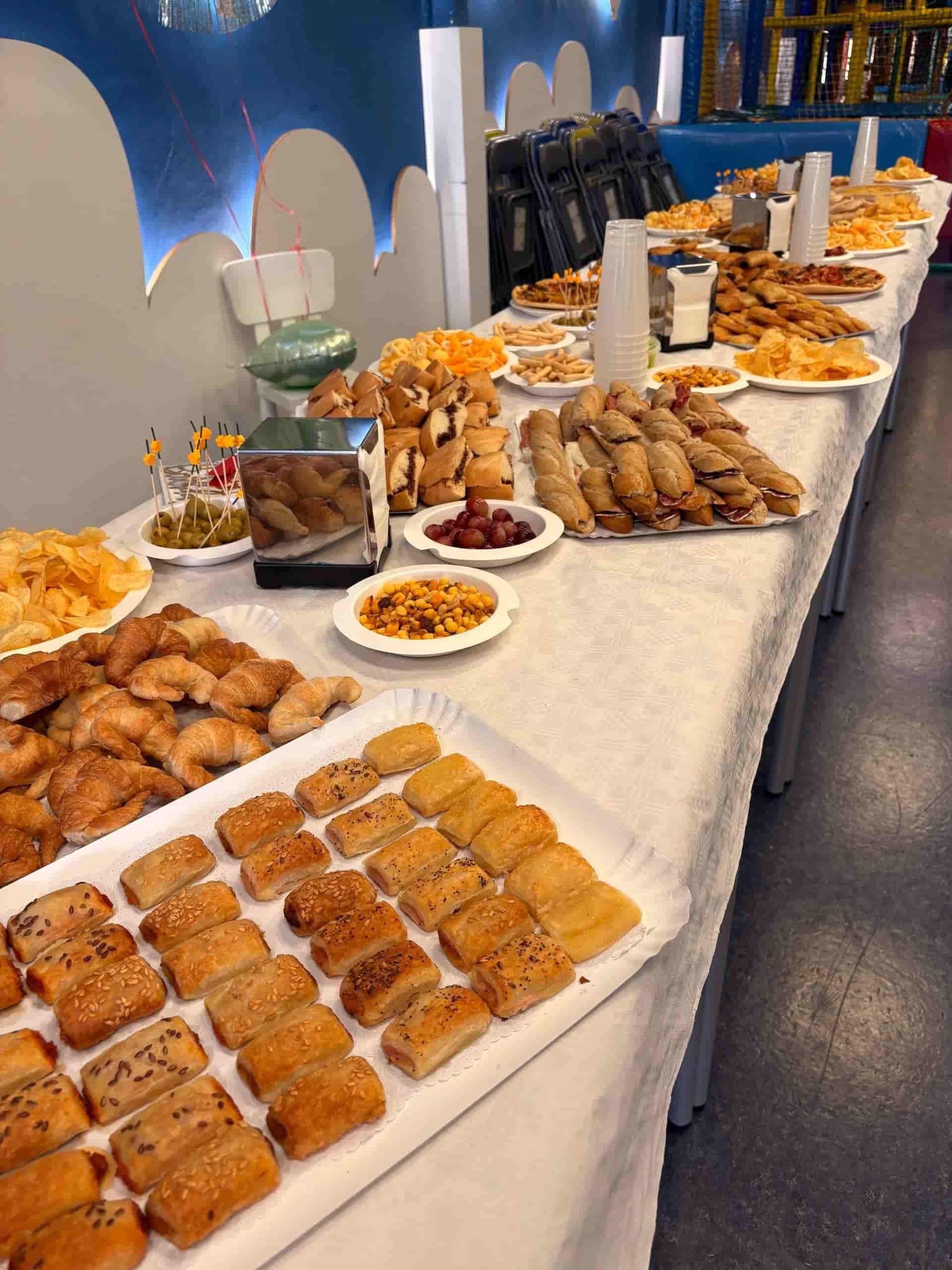 Mesa de buffet con variedad de alimentos como pasteles, panecillos, patatas fritas y aperitivos en un área de juegos de colores brillantes.