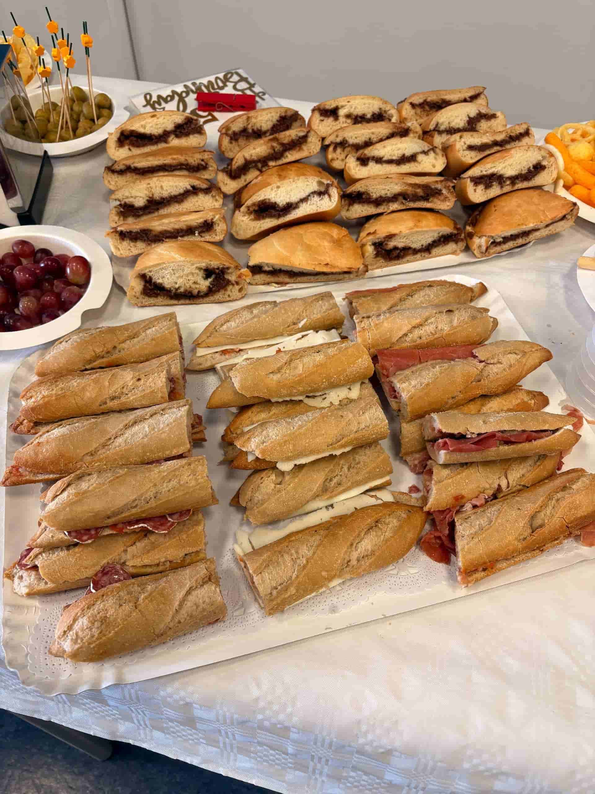 Sándwiches y snacks en una mesa: bocadillos variados, uvas, aceitunas y patatas fritas.