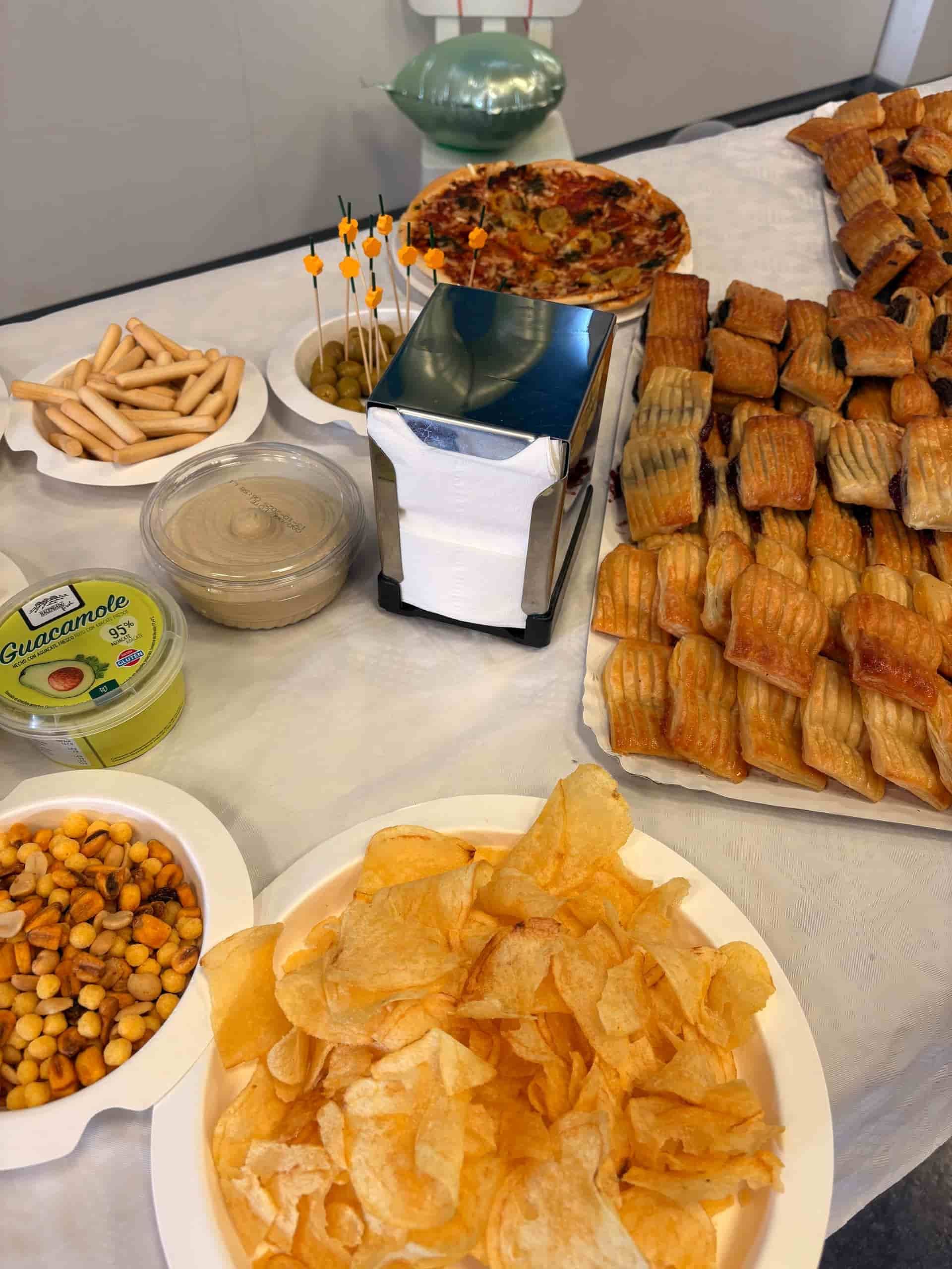 Mesa servida con diversos alimentos para fiestas: patatas fritas, hummus, quiche, hojaldres y mucho más.
