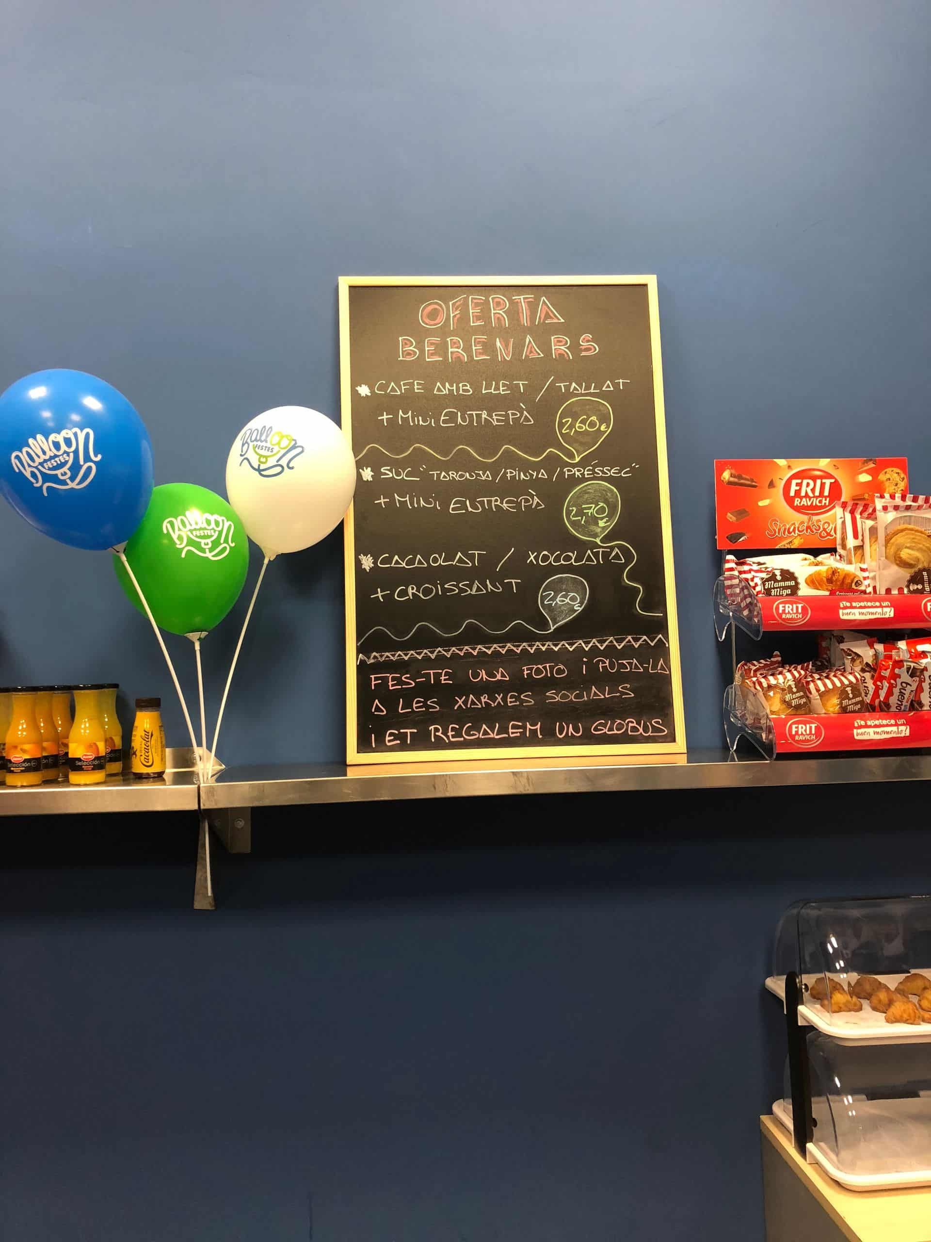 Pared azul con menú de pizarra, globos, bocadillos y bebidas exhibidos en un estante.