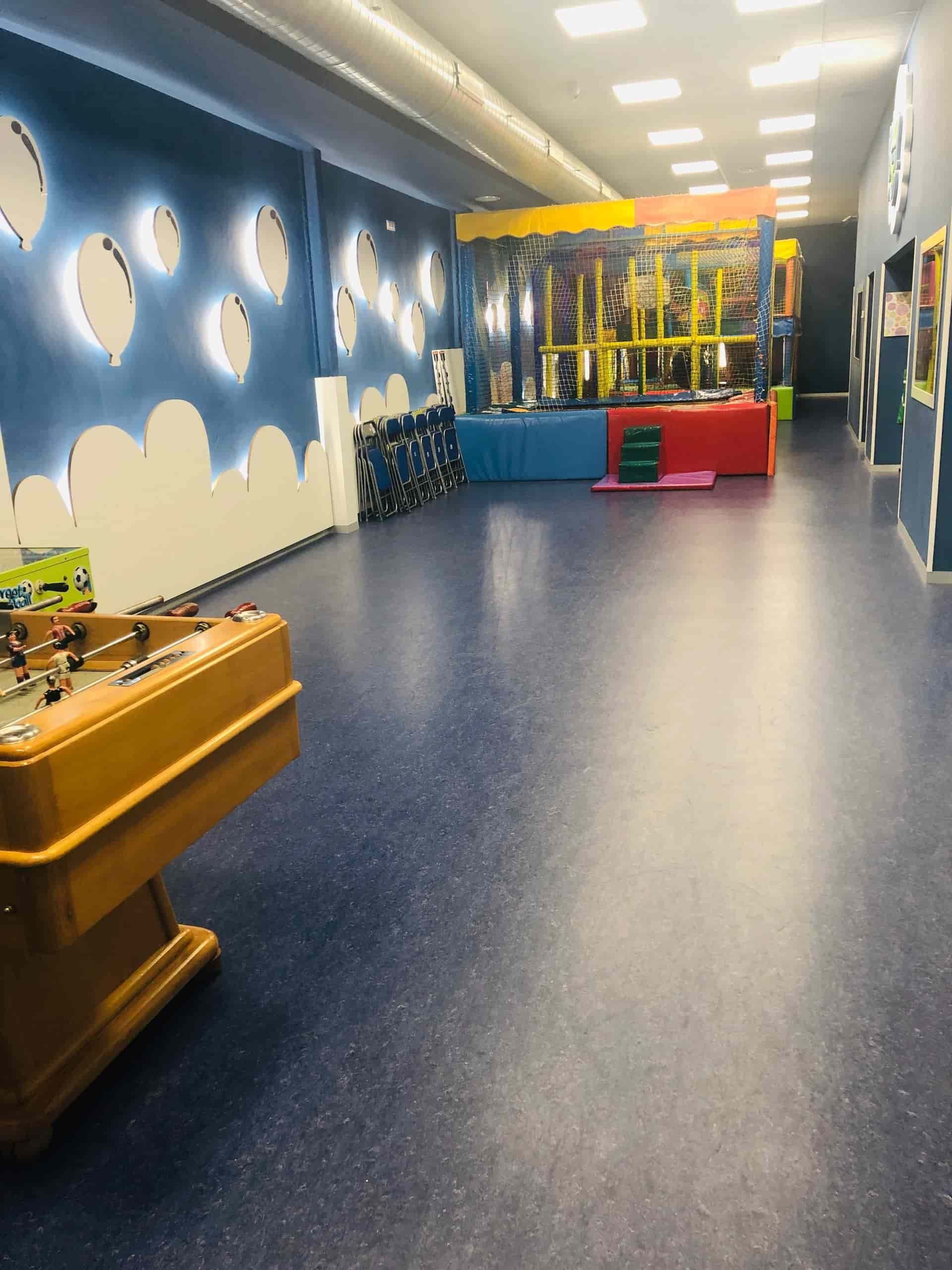 Sala de juegos interior con mesa de futbolín, paredes azules con diseños de nubes y estructura de juegos al fondo.