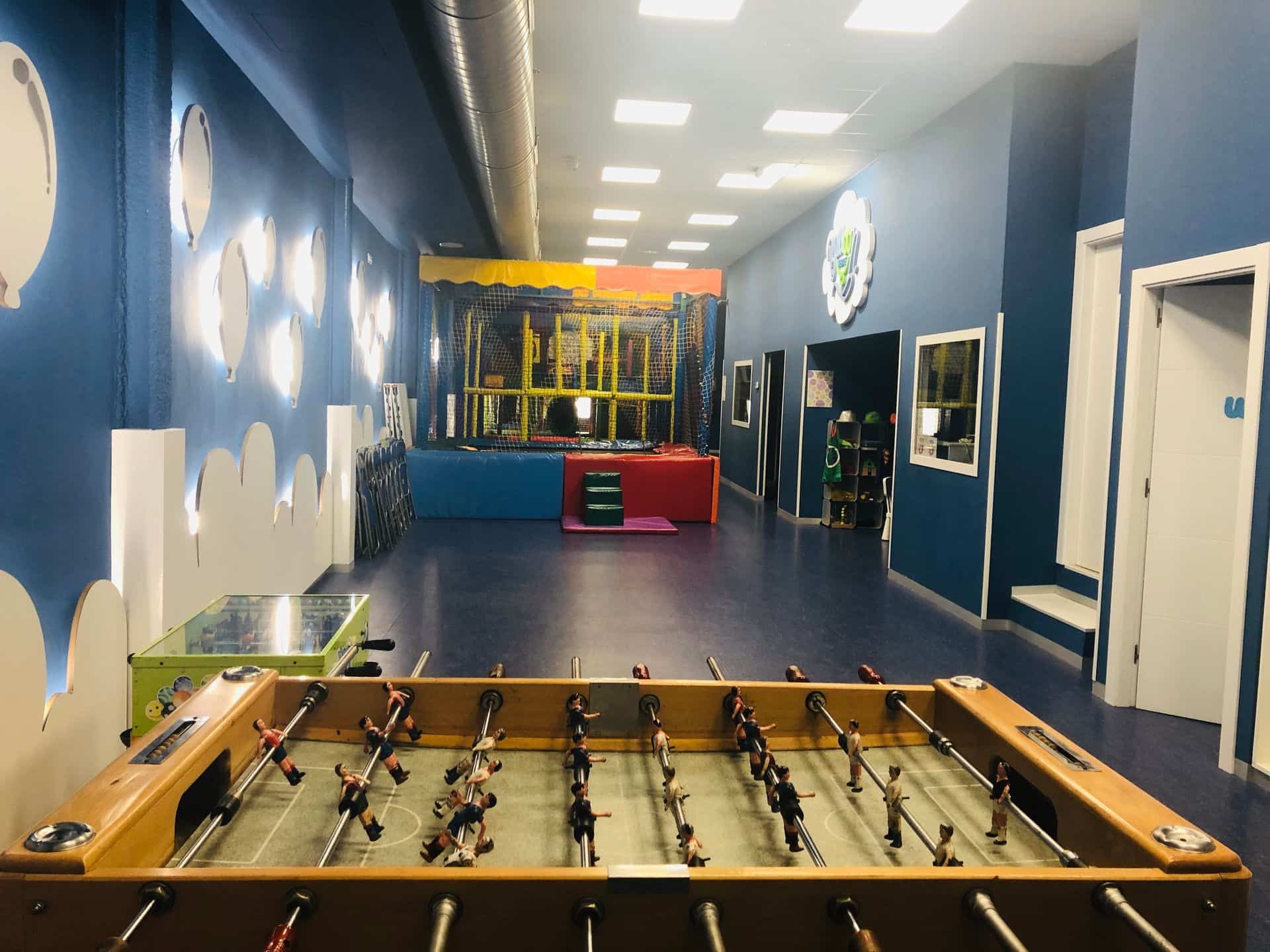 Mesa de futbolín en primer plano, que conduce a una zona de juegos infantiles con paredes azules.