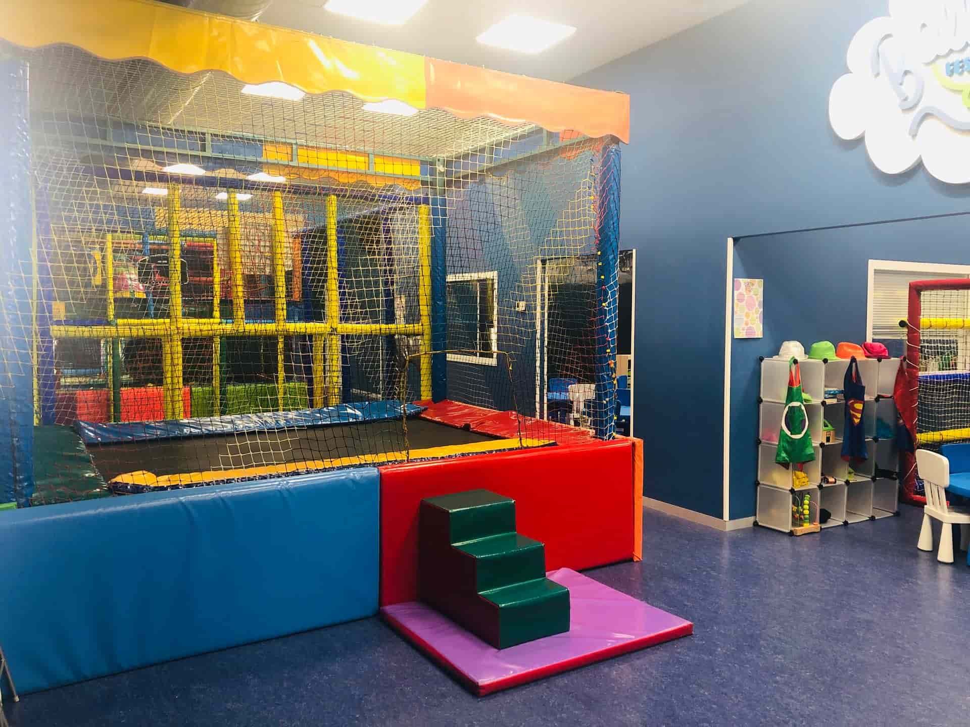 Zona de juegos interior con trampolín y estructuras acolchadas de colores.