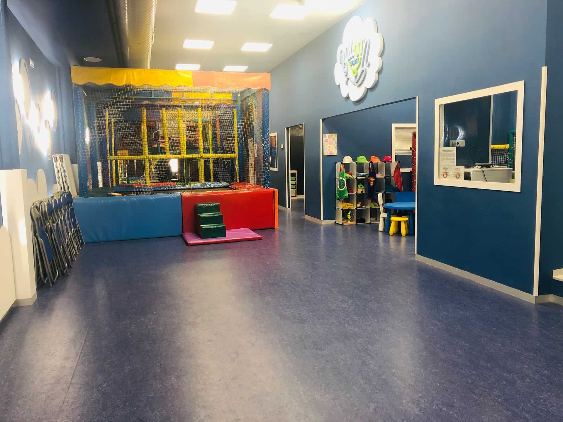 Área de juegos interior con estructura de escalada, paredes azules y equipos coloridos.