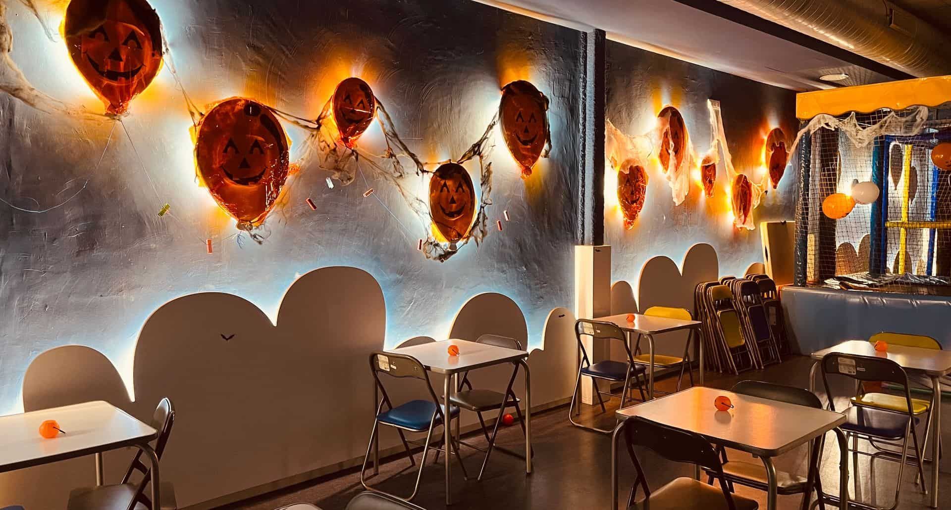 Interior de cafetería abstracta con caras surrealistas en la pared y pequeñas mesas y sillas.