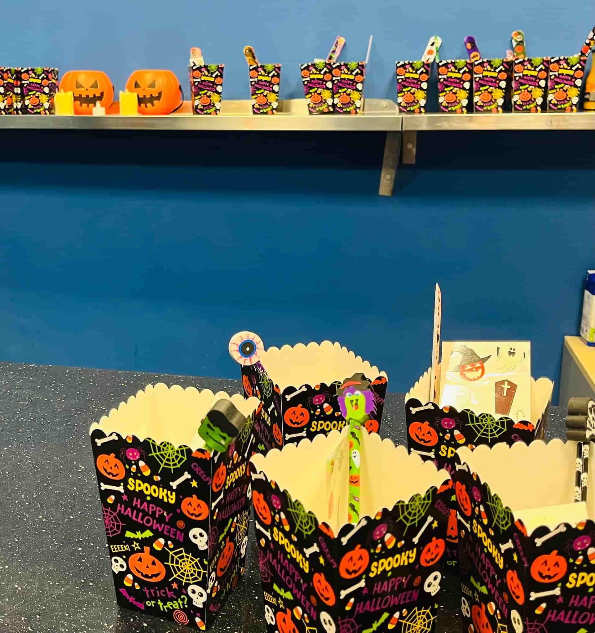 Delicias de Halloween en un estante y una mesa: cajas de palomitas de maíz, tazas y calabazas talladas.