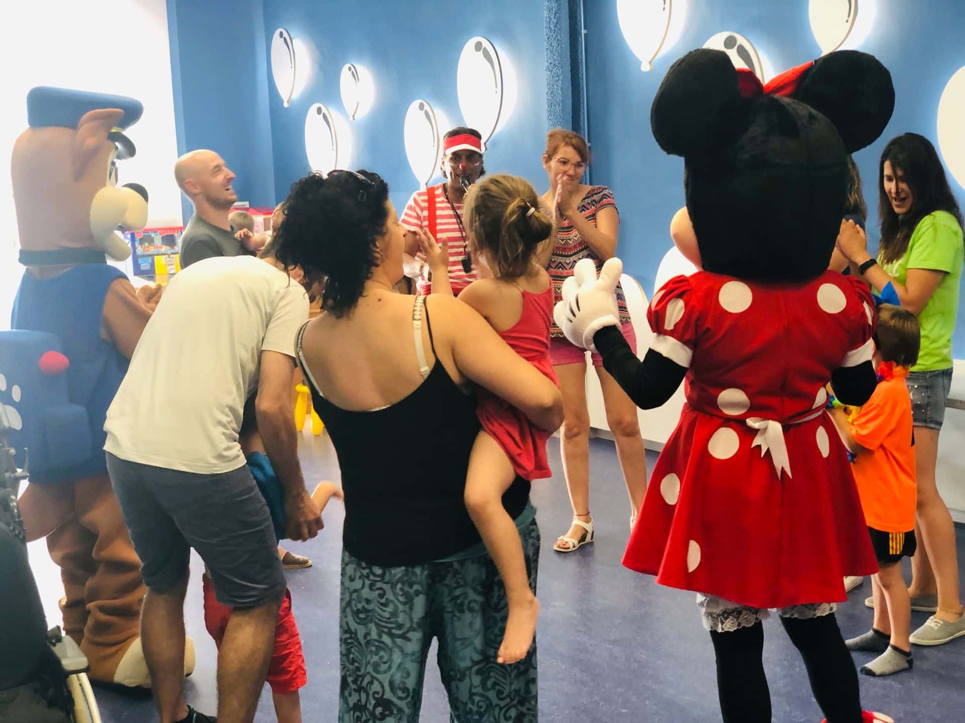 Minnie Mouse y un perro mascota interactúan con un grupo de personas. Un niño está en brazos. Habitación luminosa.