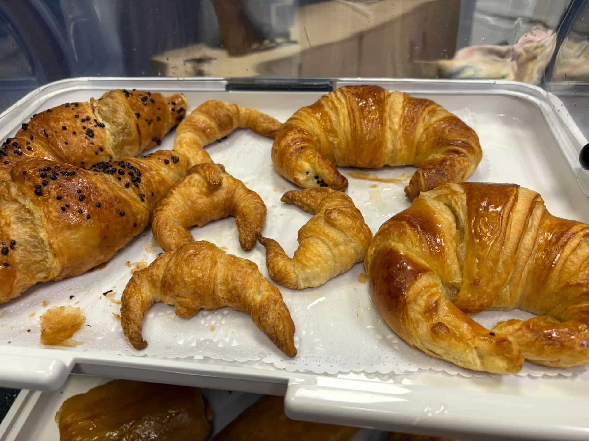 Croissants en una bandeja blanca; algunos están cubiertos de chocolate y todos son de color marrón dorado y hojaldrados.