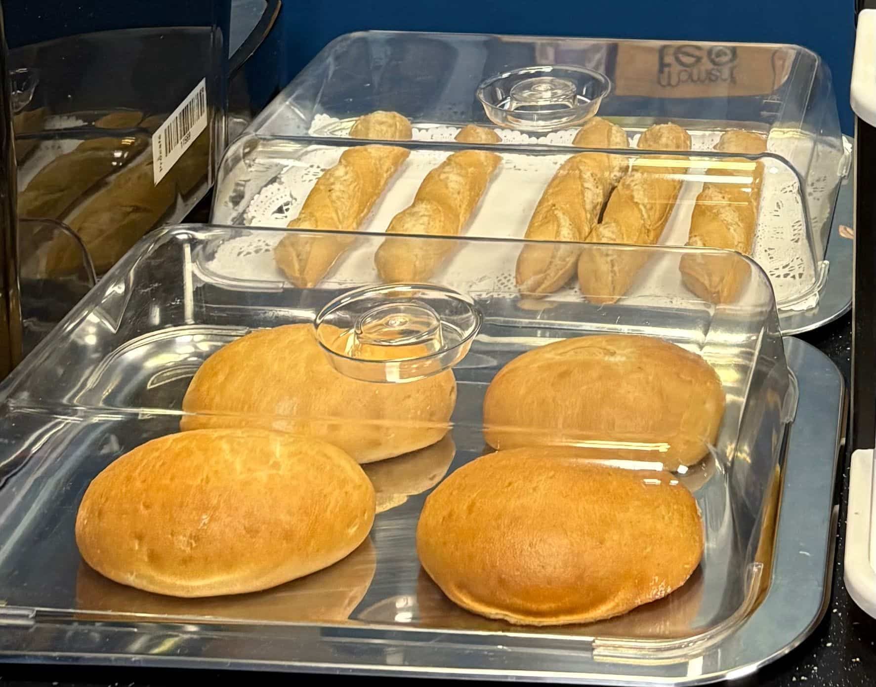 Panecillos y baguettes en bandejas, bajo tapas transparentes, listos para servir.