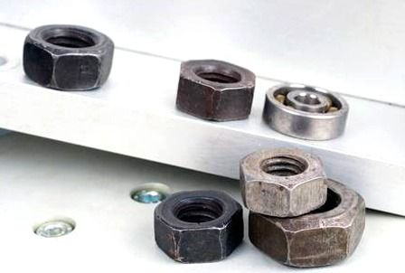 Las tuercas y los tornillos se apilan uno encima del otro sobre una superficie blanca.