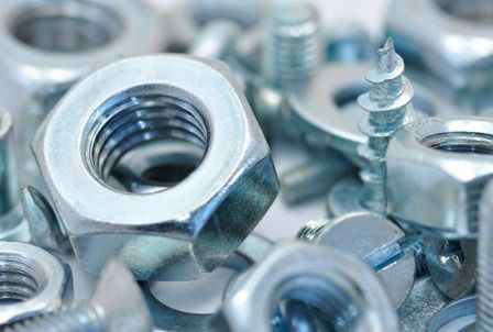 Un montón de tuercas y tornillos sobre una superficie blanca.