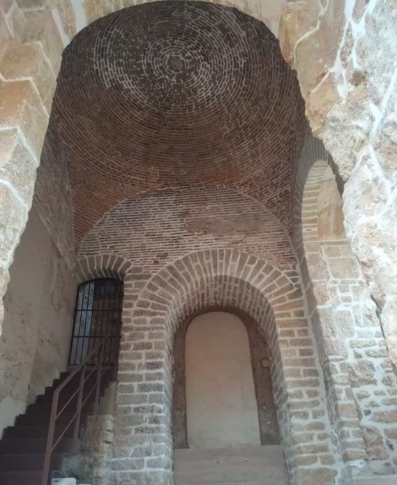 Nicho abovedado de piedra con techo de cúpula de ladrillo y estrechas ventanas enrejadas en el interior de una antigua estructura de mampostería