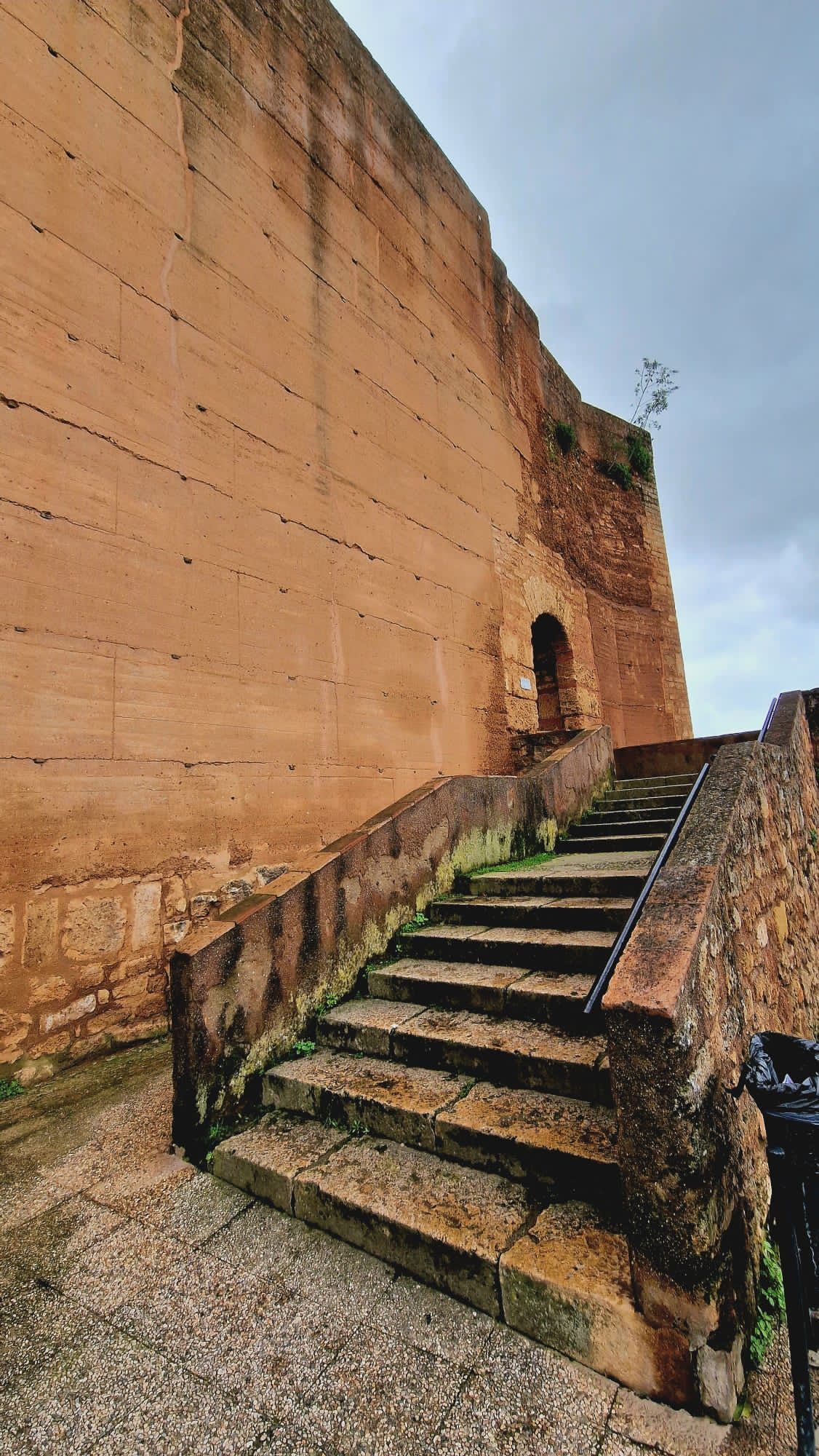 Escalera de piedra junto a una alta muralla de fortaleza color arena bajo un cielo azul