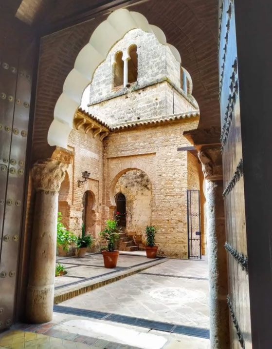 Patio de piedra ornamentado con arcos, plantas en macetas y arquitectura morisca tallada bajo una cálida luz solar