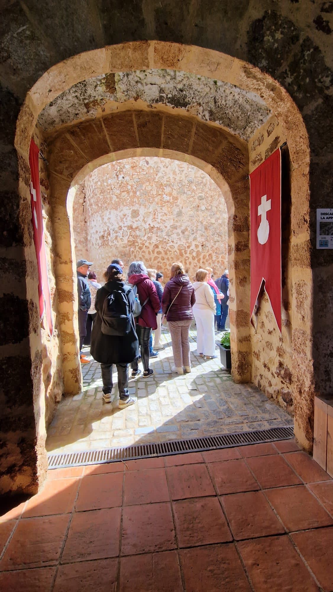 Los turistas se reunieron bajo un arco de piedra y contemplaron un patio luminoso con estandartes rojos.