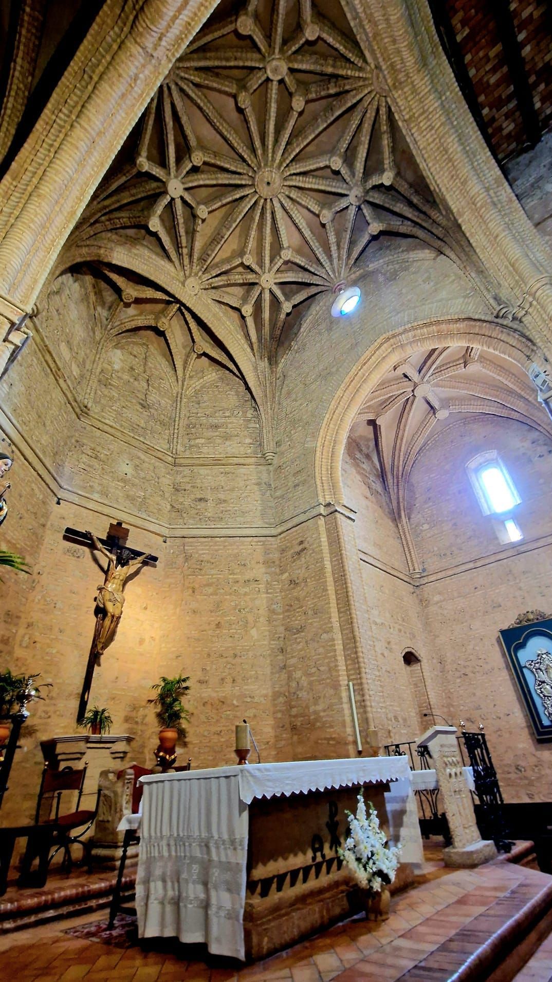 Altar de una iglesia gótica bajo un techo abovedado de piedra, con un crucifijo y vidrieras emplomadas