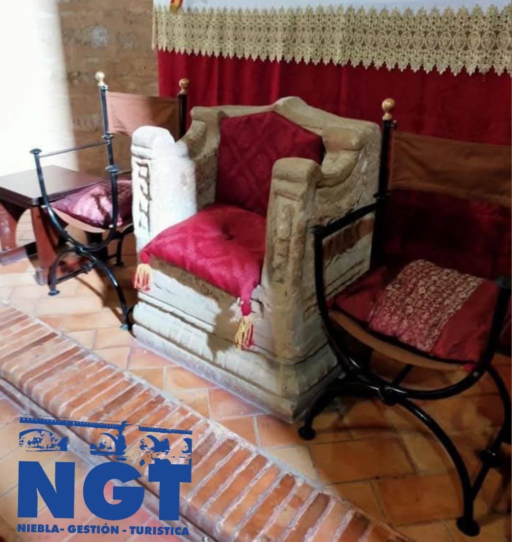 Silla tapizada roja con reposabrazos beige y mesas auxiliares de metal negro sobre un suelo de baldosas, en una habitación