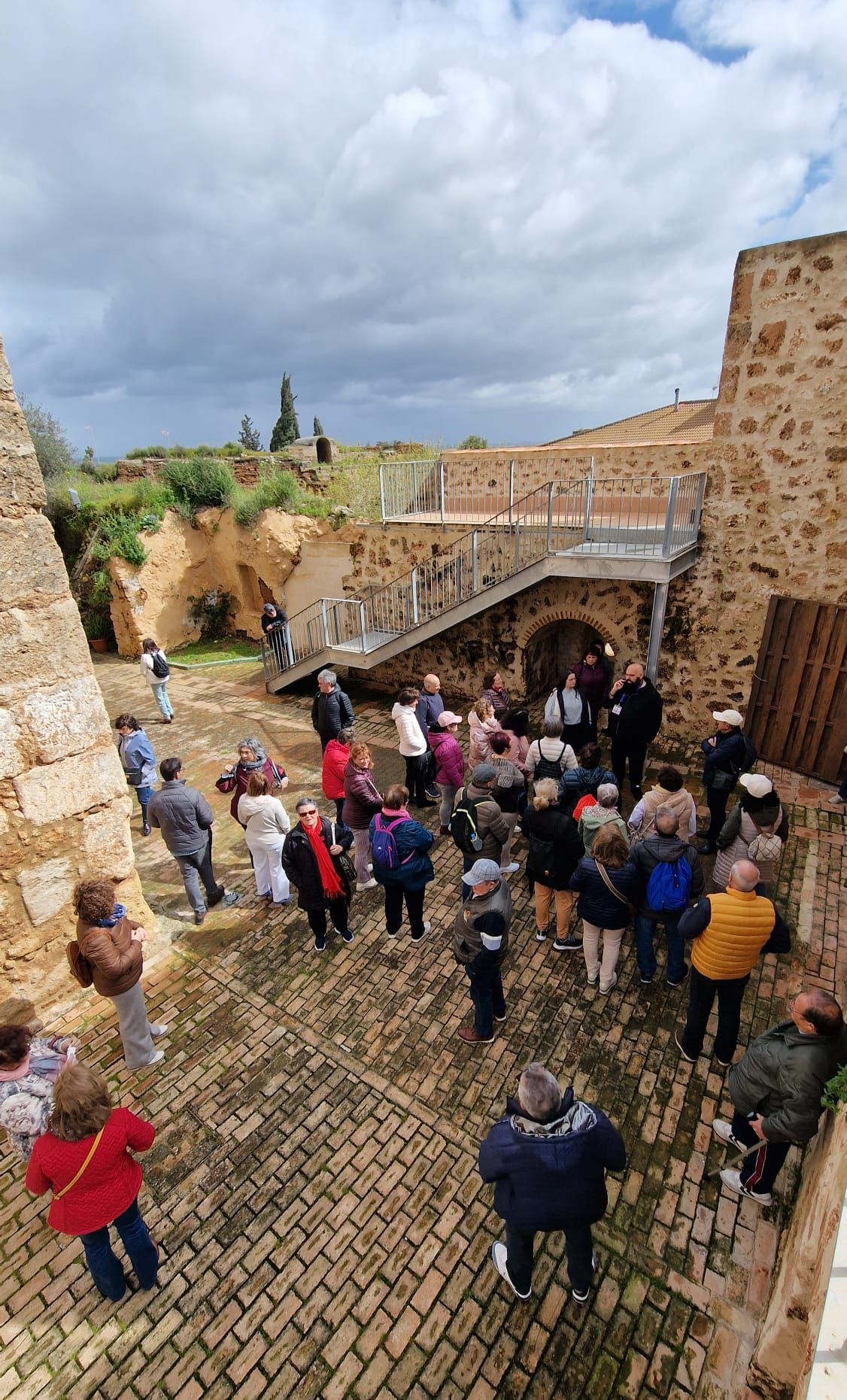 Una multitud de turistas en un camino empedrado junto a unas ruinas de piedra, bajo un cielo nublado