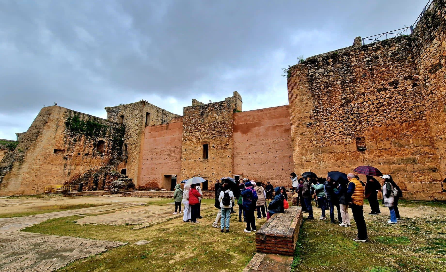 Turistas recorriendo las ruinas de una gran fortaleza de piedra bajo un cielo nublado