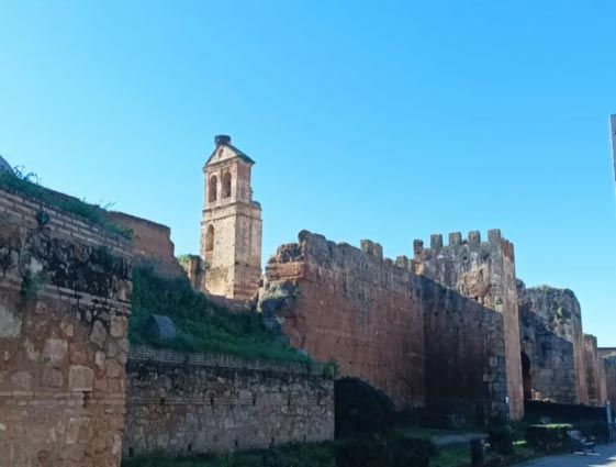 Murallas de una fortaleza de piedra y una torre alta bajo un cielo azul brillante.