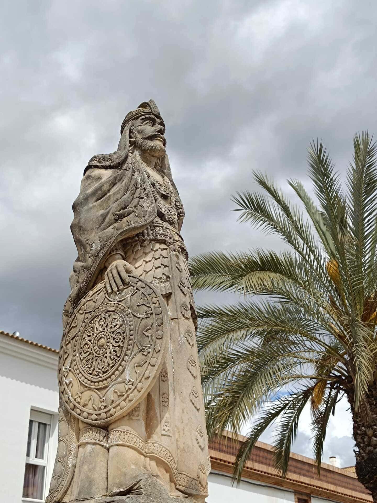 Estatua de piedra junto a una palmera, bajo un cielo nublado