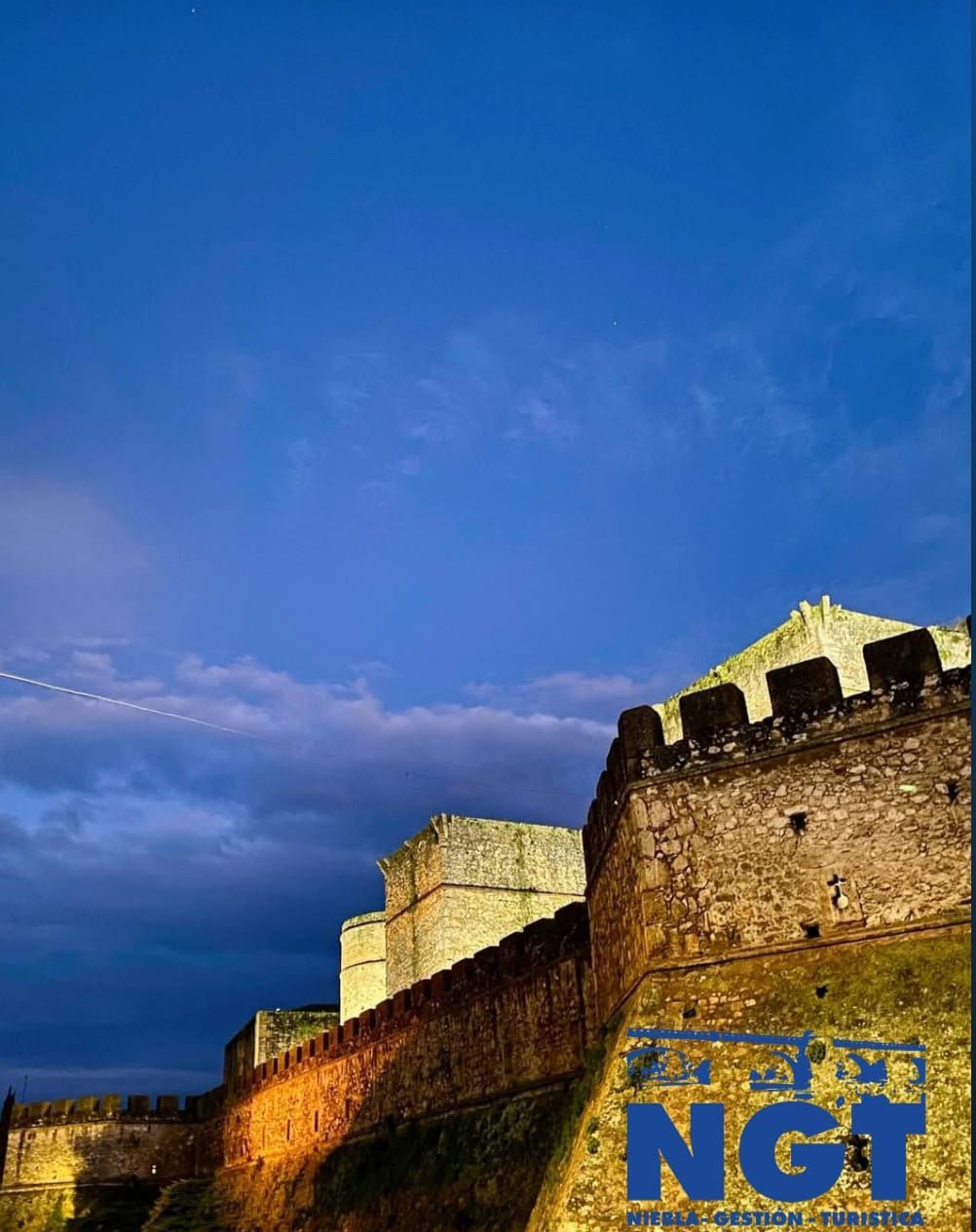Muralla de piedra iluminada bajo un cielo azul al atardecer