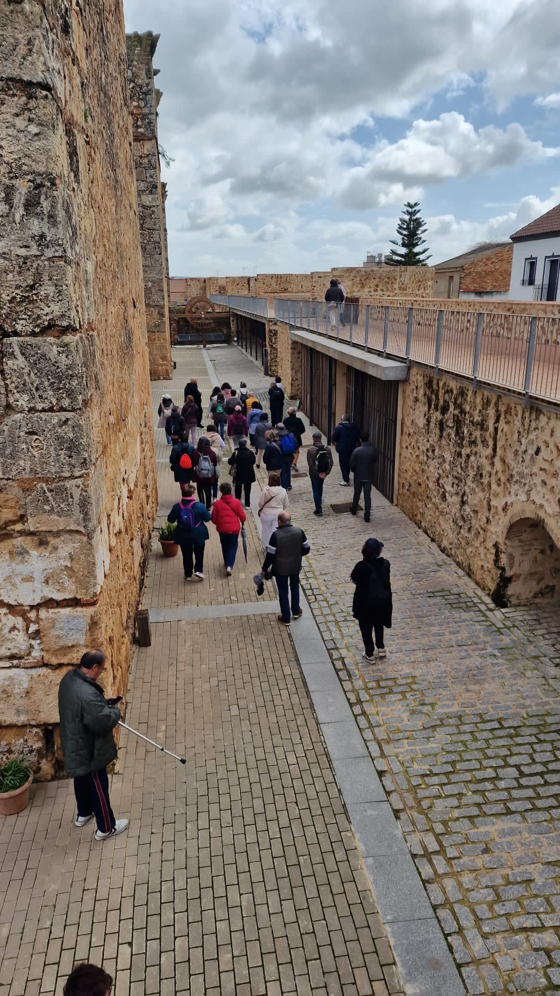 Turistas caminando por un sendero empedrado entre muros de piedra en una fortaleza histórica bajo un cielo nublado