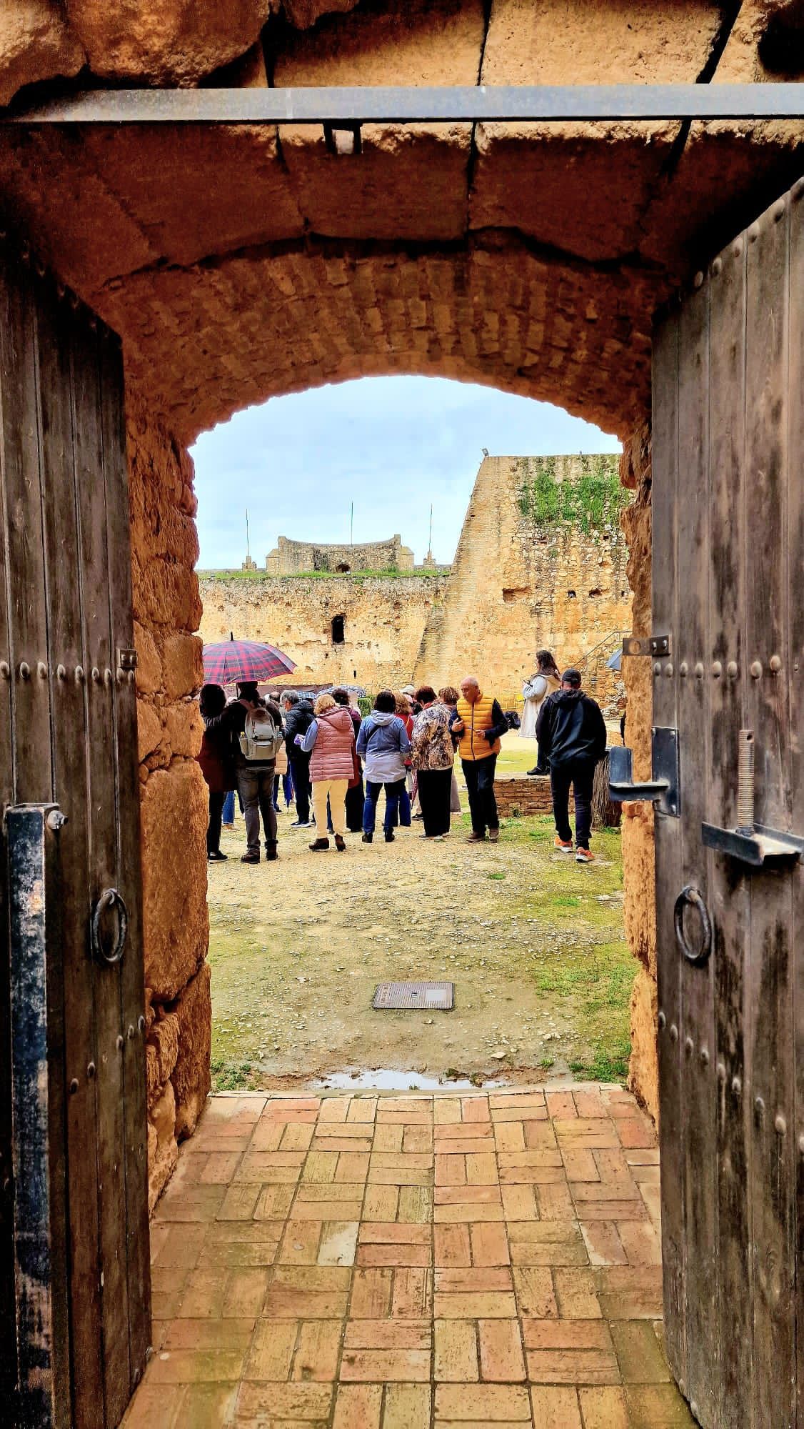 Personas de pie frente a un arco histórico de ladrillo, vistas a través de unas puertas de madera abiertas.